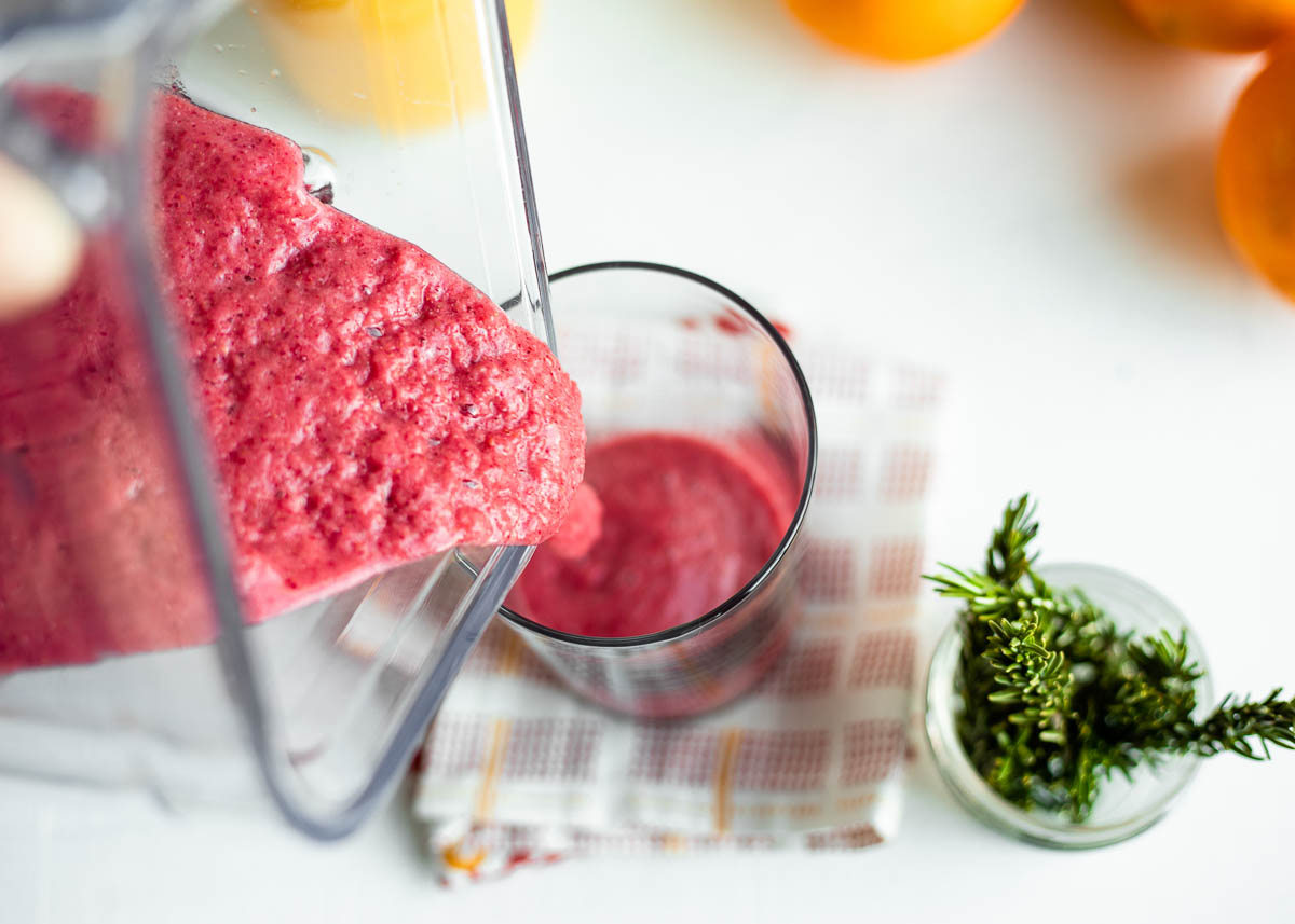 blender container pouring pink smoothie into a glass on a tea towel. 