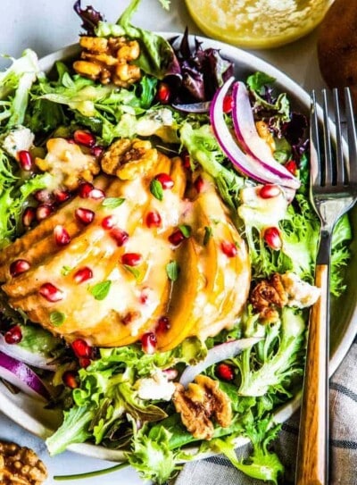 winter pear salad with roasted pear dressing topped with pomegranate arils on a circle plat with a fork.