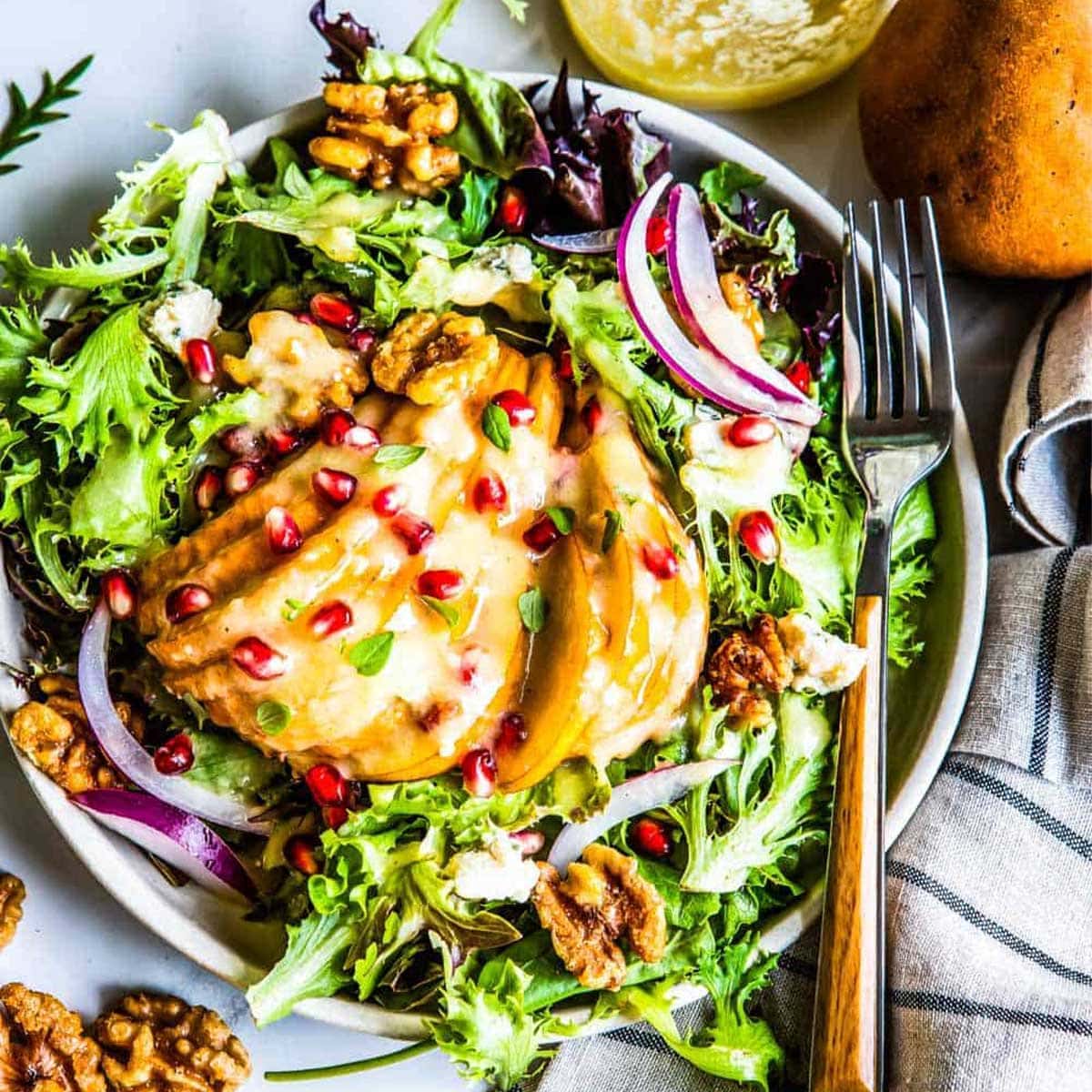 winter pear salad with roasted pear dressing topped with pomegranate arils on a circle plat with a fork.