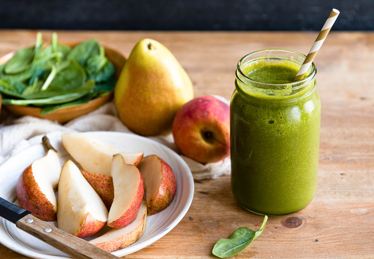 pear smoothie in a glass jar with a paper straw next to a plate of pear slices.