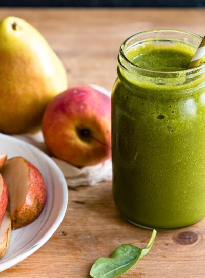 green pear smoothie in a mason jar with a paper straw, next to some sliced and whole pears.