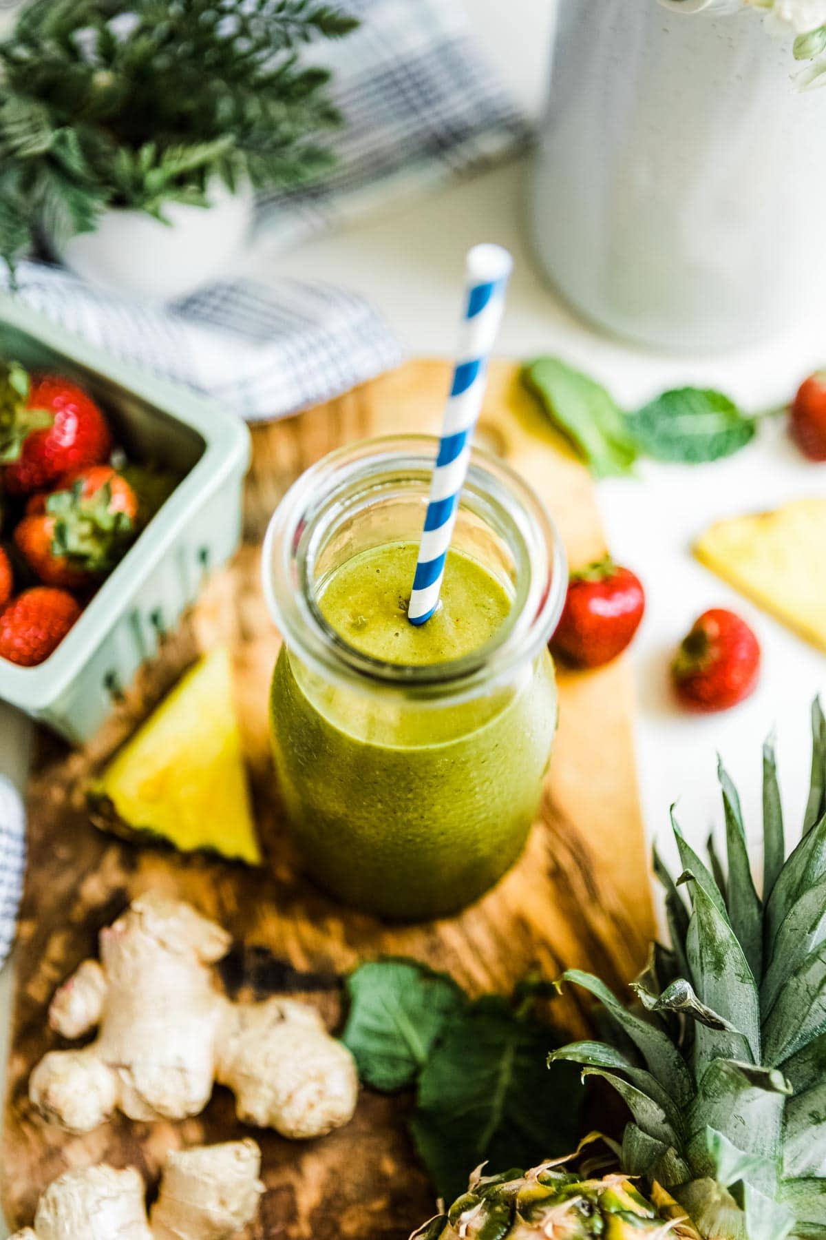 pineapple ginger smoothie in a glass jar with a blue and white striped paper straw.