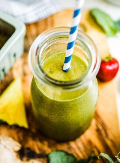 pineapple ginger smoothie in glass jar with blue and white striped paper straw.