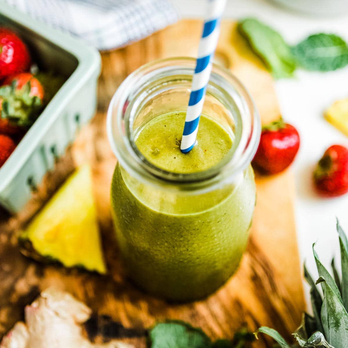 pineapple ginger smoothie in glass jar with blue and white striped paper straw.