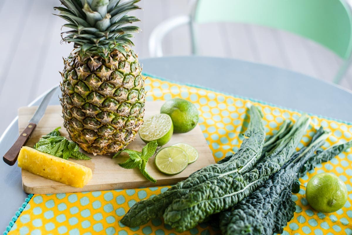 ingredients for a tropical smoothie recipe including pineapple, lime, mint and kale.