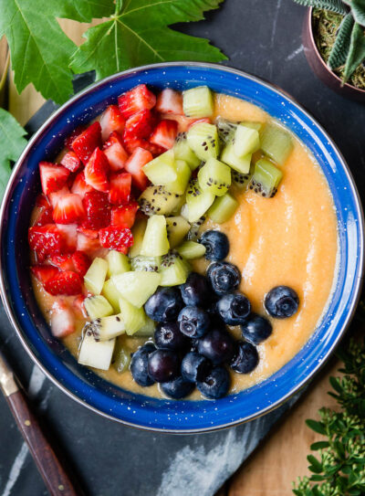 bright blue bowl of orange smoothie topped with fresh fruit.