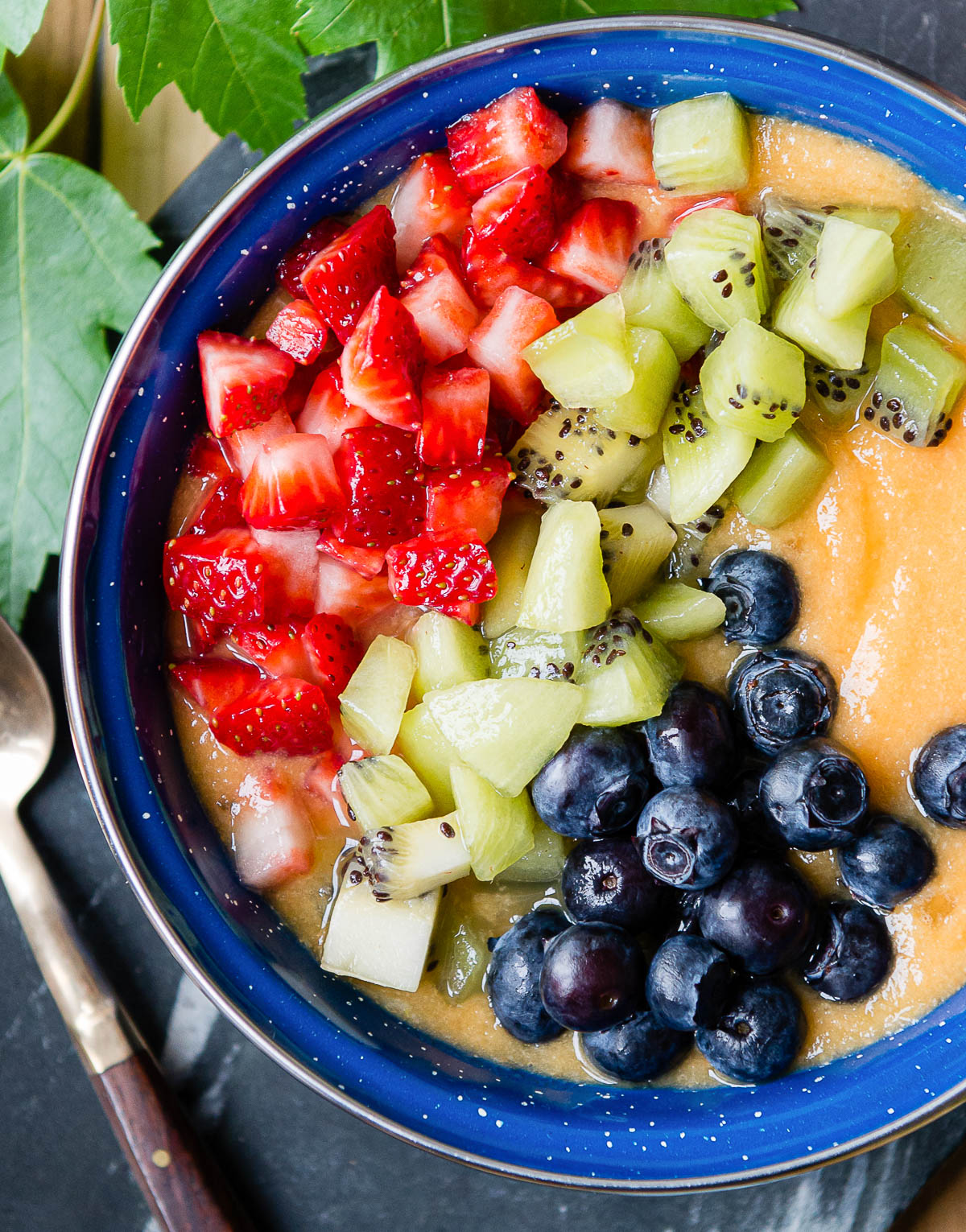 sliced strawberries, kiwi and blueberries on top of a thick orange smoothie.