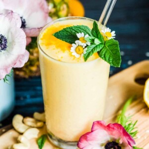 Pineapple smoothie in a glass with a glass straw and mint garnish.