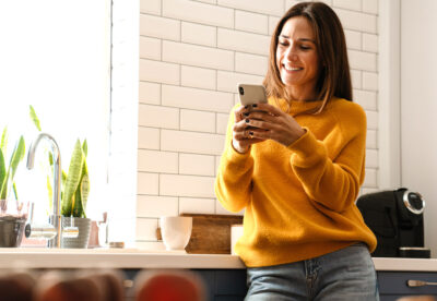 Woman looking at her phone while leaning on the counter and smiling.