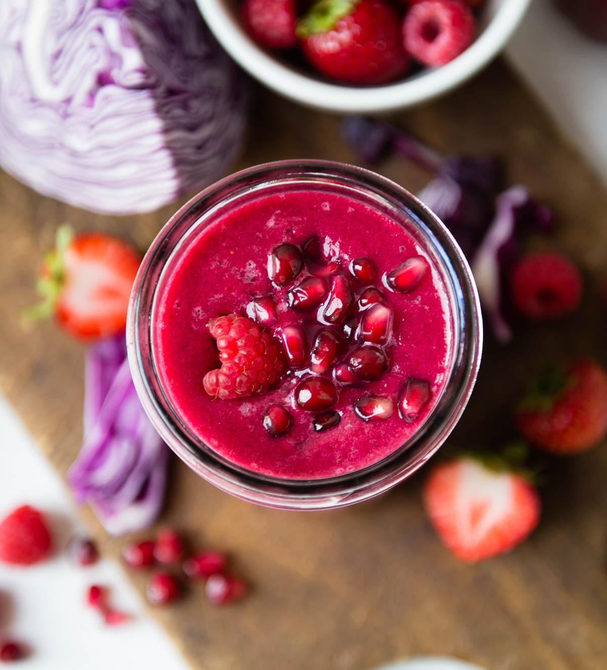 Glass jar full of fruit smoothie topped with red fruits.