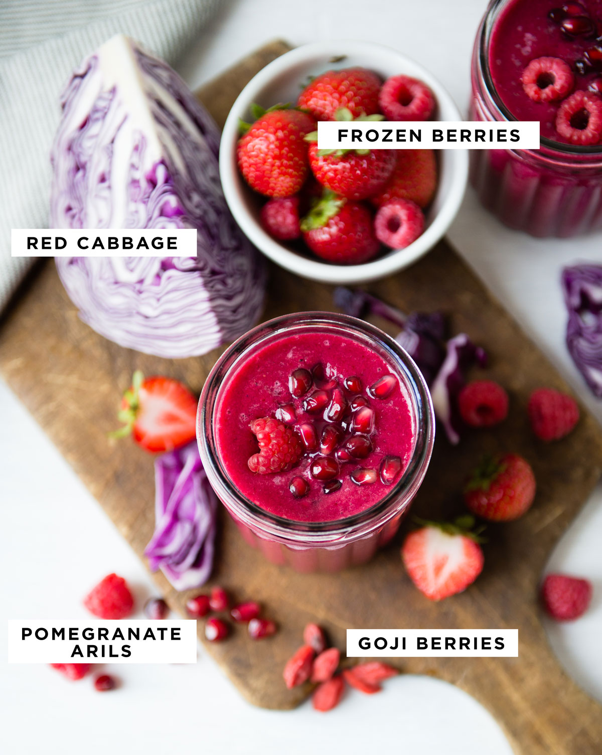 Labeled ingredients for a red pomegranate smoothie including frozen berries, red cabbage, pomegranate arils and goji berries.