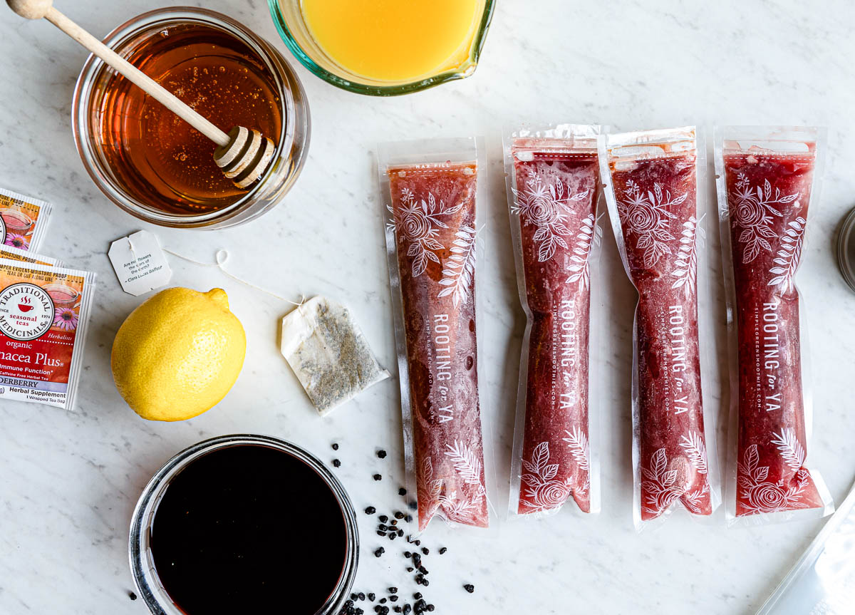 4 frozen popsicle sleeves next to the ingredients in them including honey, herbal tea, lemon and elderberry syrup.