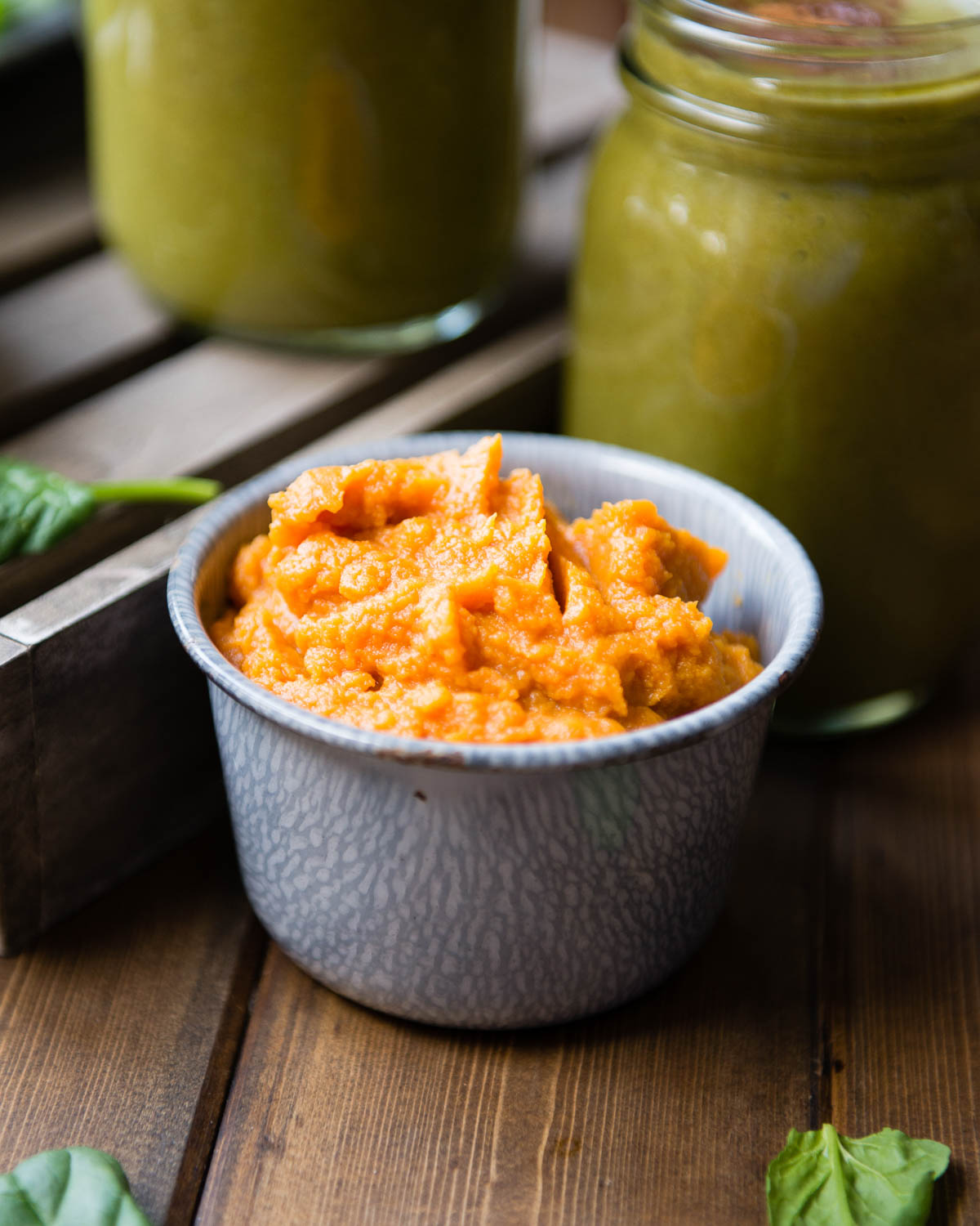 A tin bowl full of pumpkin puree, surrounded by blurred glass mugs full of the pumpkin smoothie. 