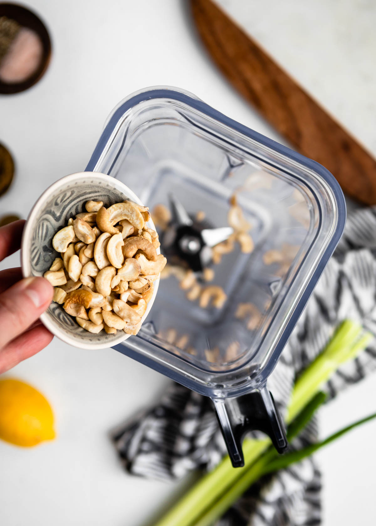 pouring cashews from a small bowl into a blender container.