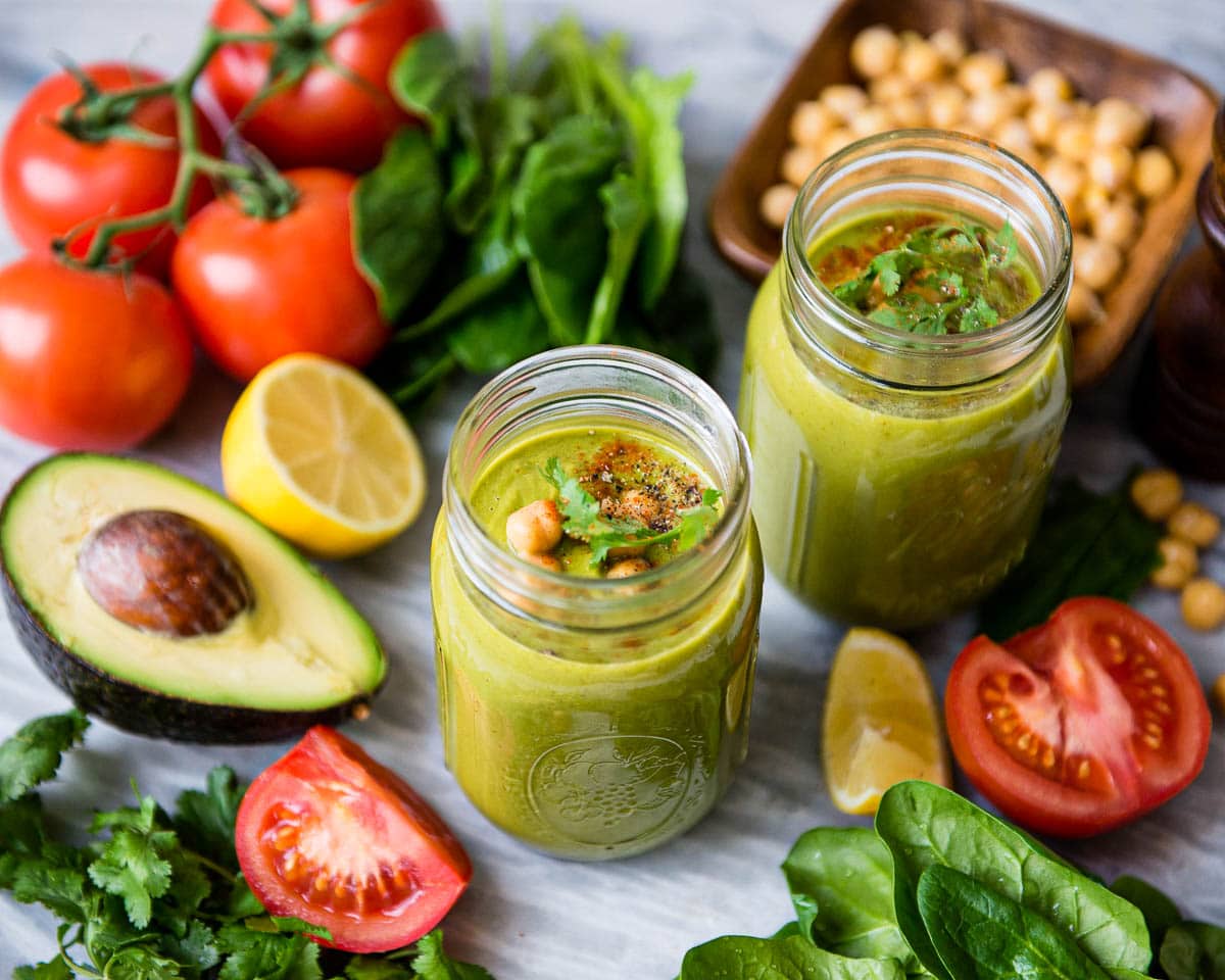 2 savory meal replacement smoothies in glass jars surrounded by vegetables that are low in sugar and not sweet.