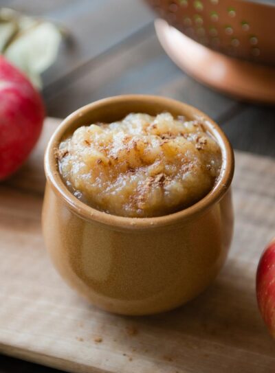 brown ceramic bowl full of slow cooker applesauce topped with cinnamon sitting on a wooden cutting board.