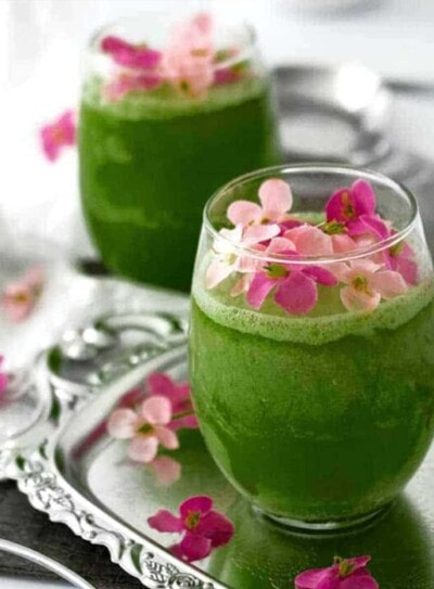 green smoothie for pregnancy in a round glass topped with pink flowers and sitting on a silver tray.