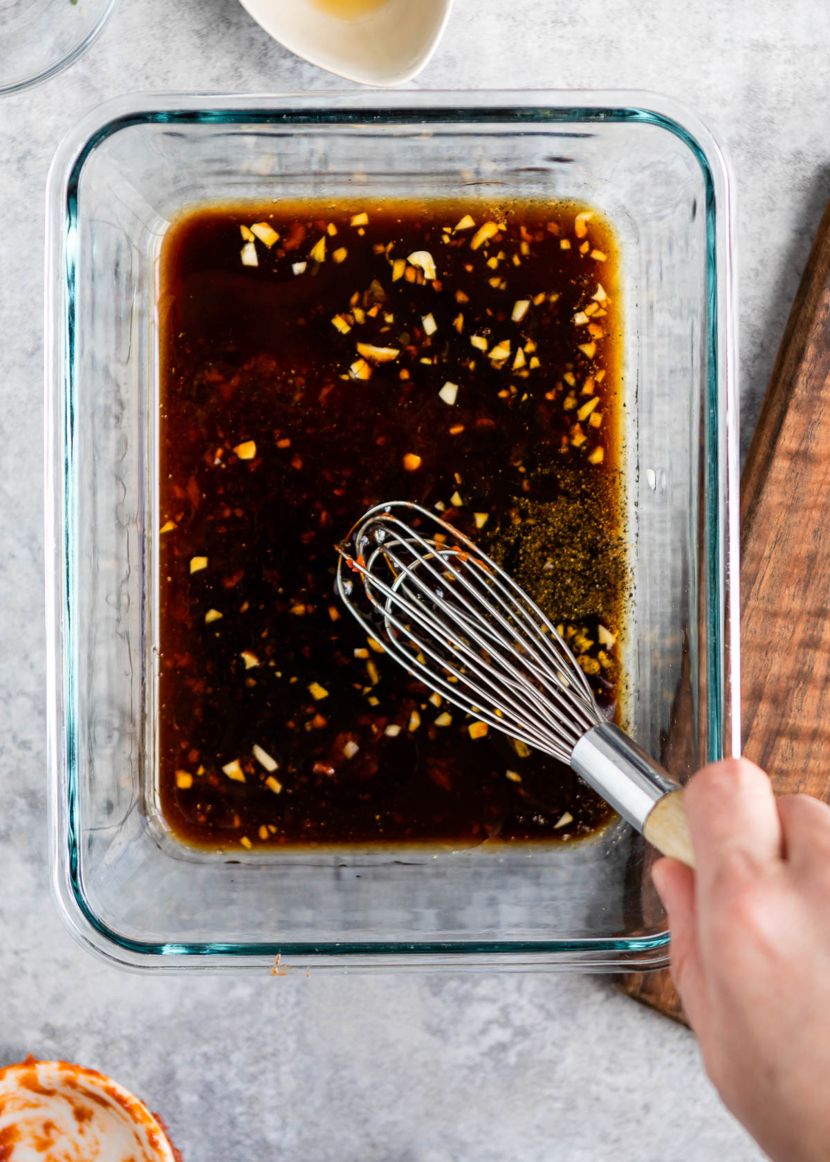 one hand with a wire whisk whisking a marinade in a glass dish.