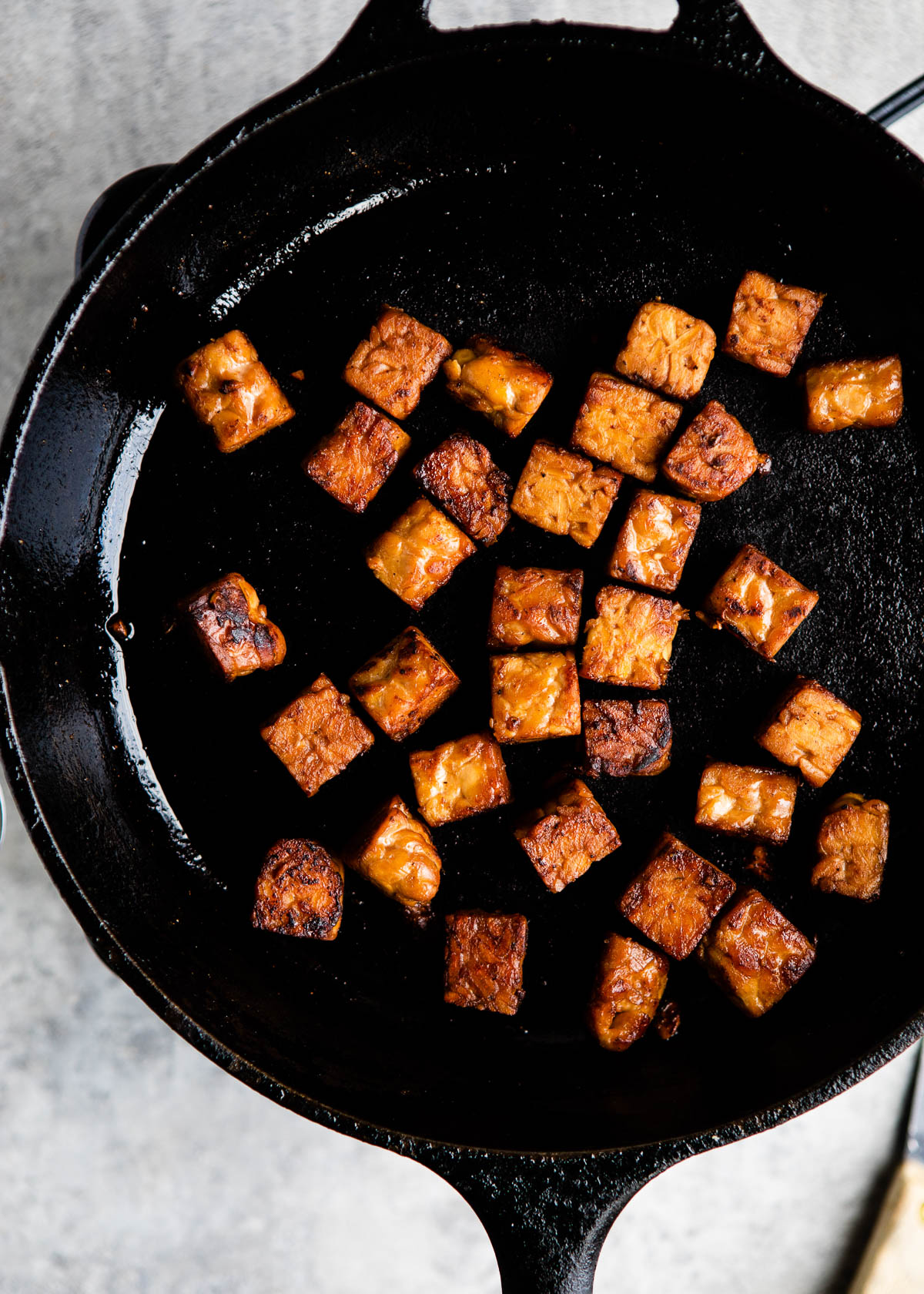 black skillet with pieces of fried marinated tempeh squares.