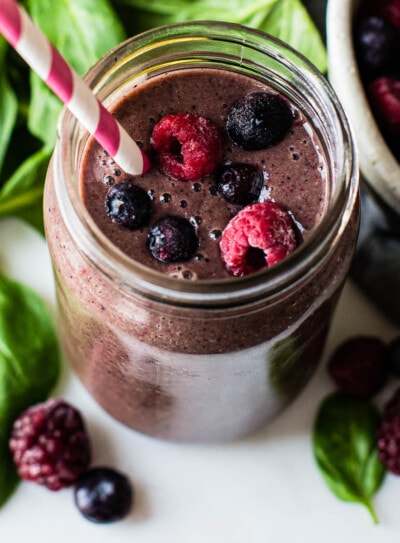 Overhead photo of a spinach berry smoothie topped with berries and surrounded by fresh spinach.