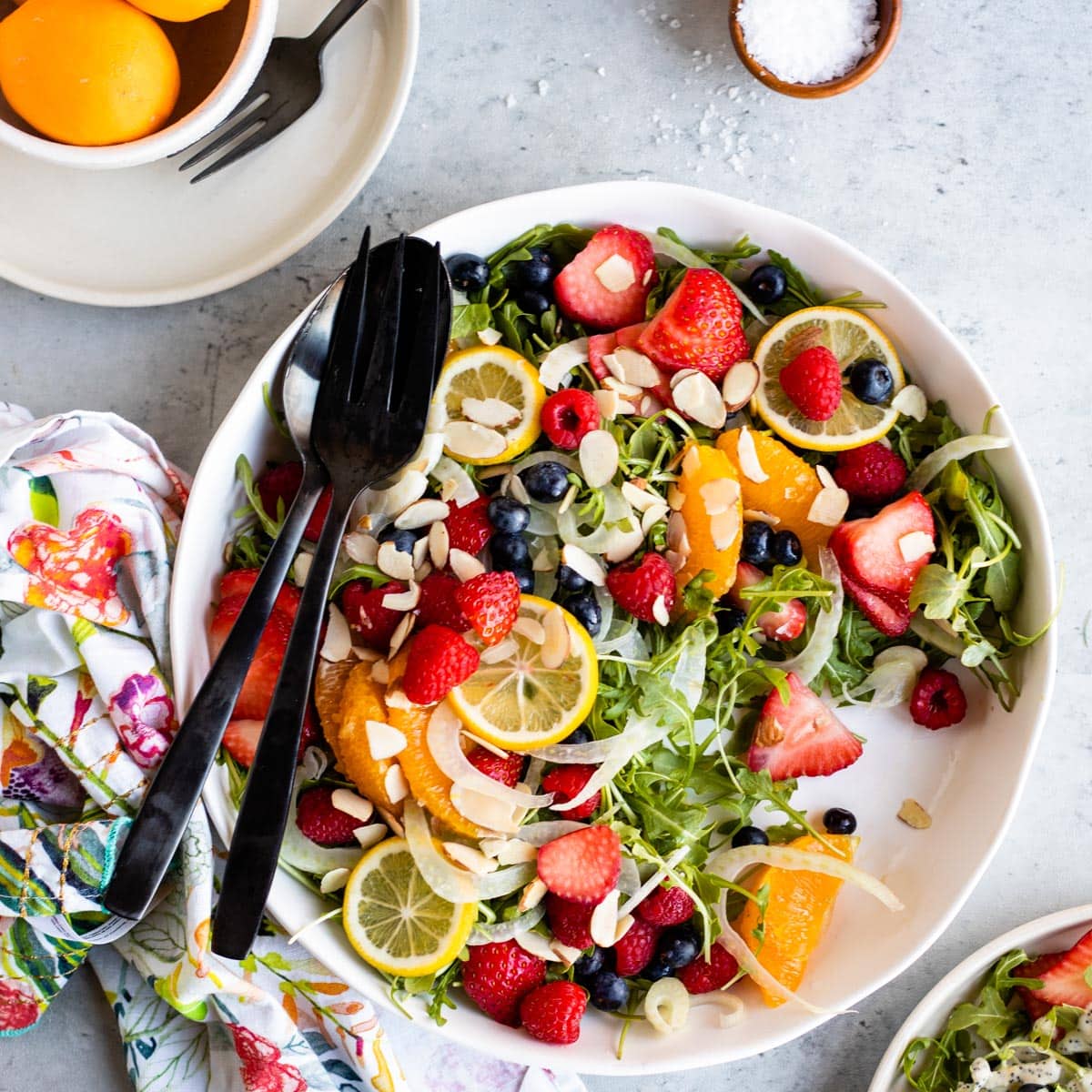 strawberry arugula salad with lemon dressing on a white plate with black utensils.