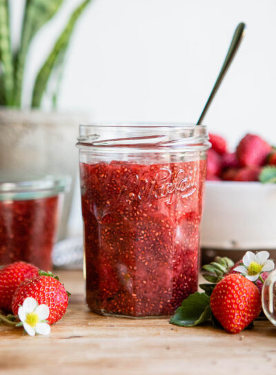 strawberry chia jam in jelly jar with spoon on counter.