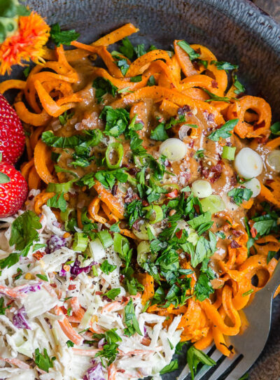 Gray bowl of Sweet Potato Noodles topped with fresh herbs, vegan coleslaw, and whole strawberries.