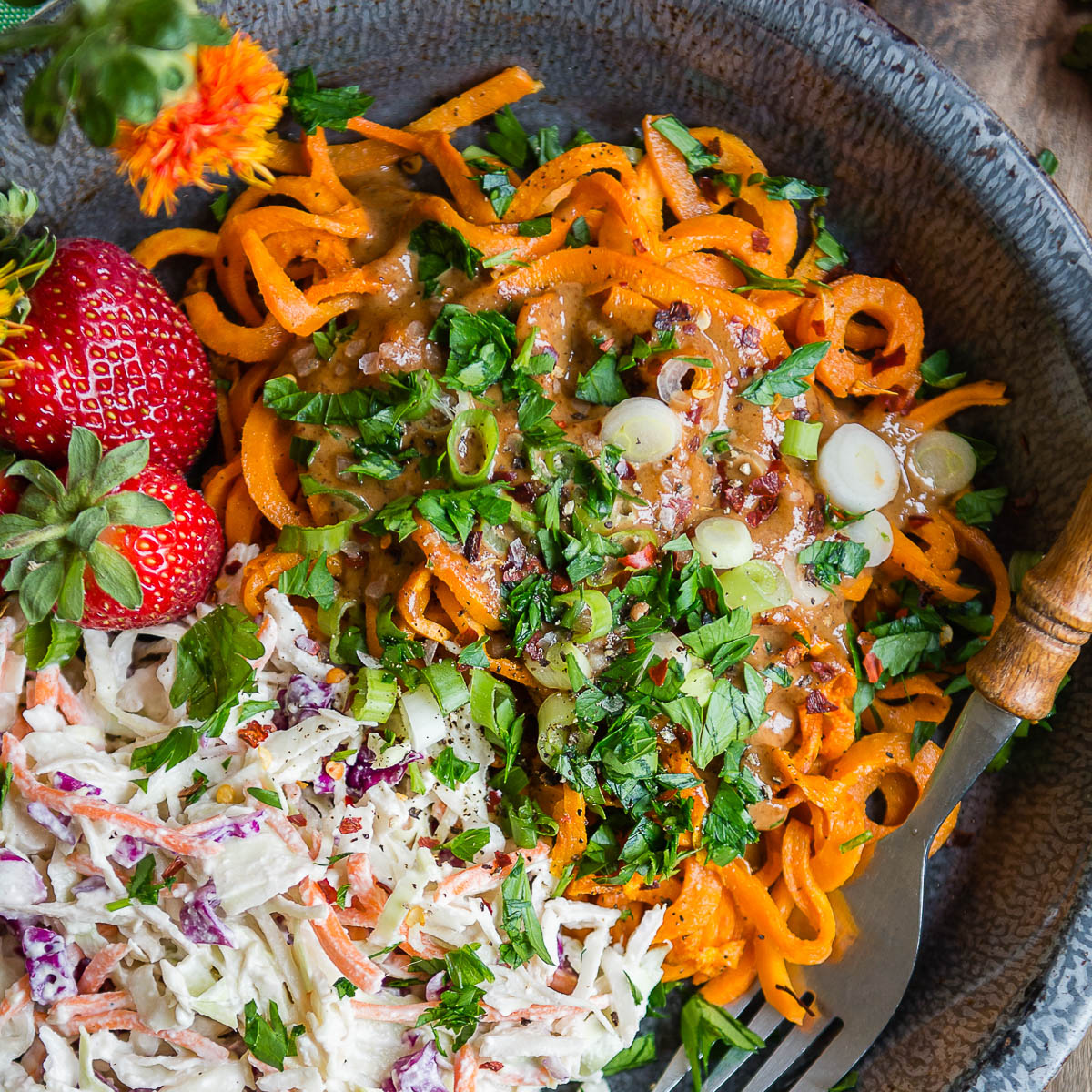 Gray bowl of Sweet Potato Noodles topped with fresh herbs, vegan coleslaw, and whole strawberries.