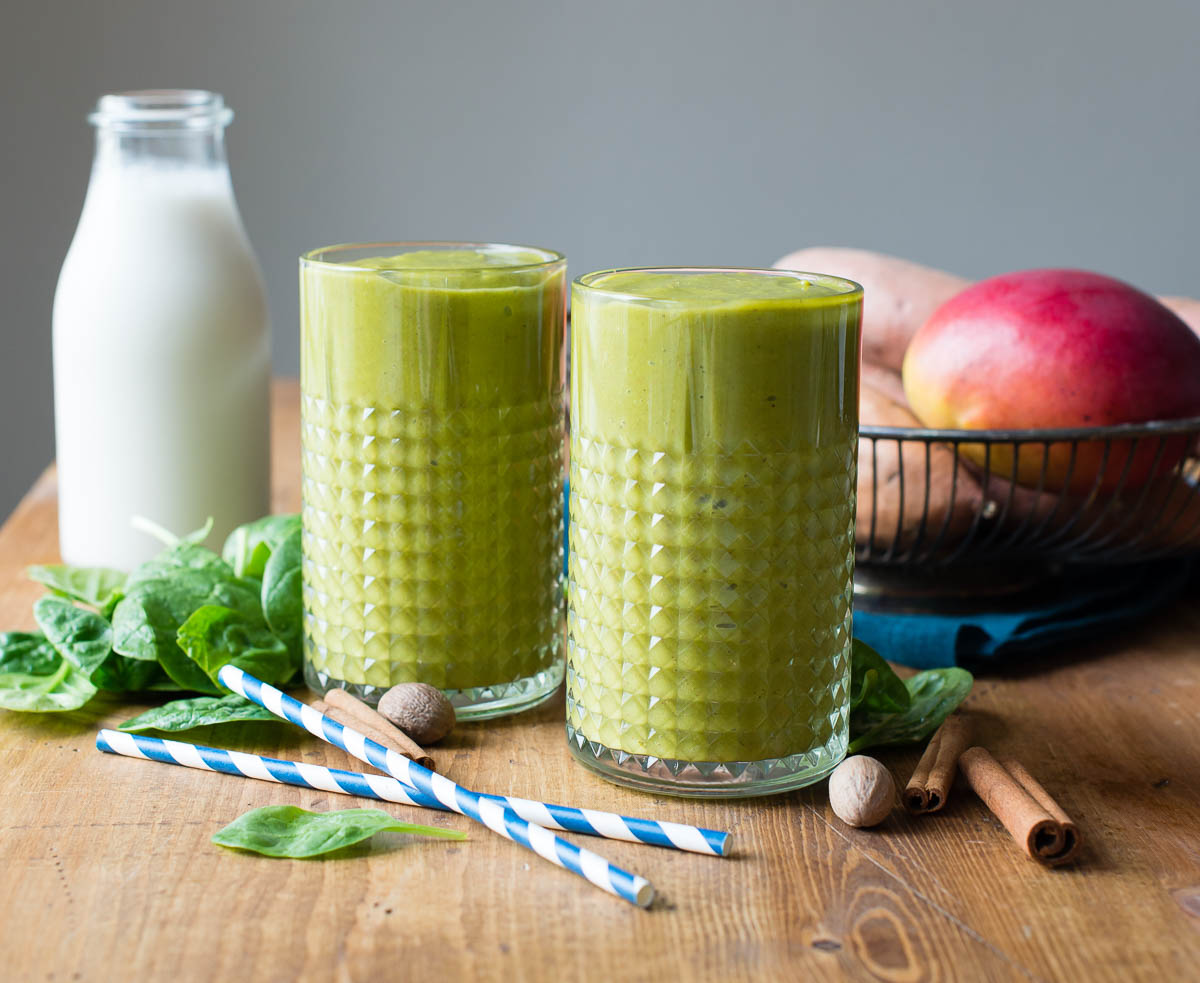 Glasses of sweet potato smoothie on a table with fresh spinach and cinnamon sticks nearby.