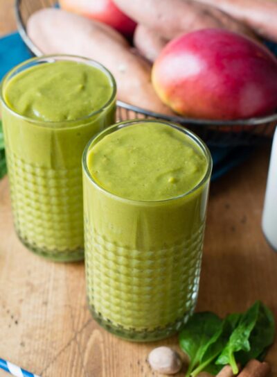 Two glasses of sweet potato smoothie on a table with fresh ingredients.