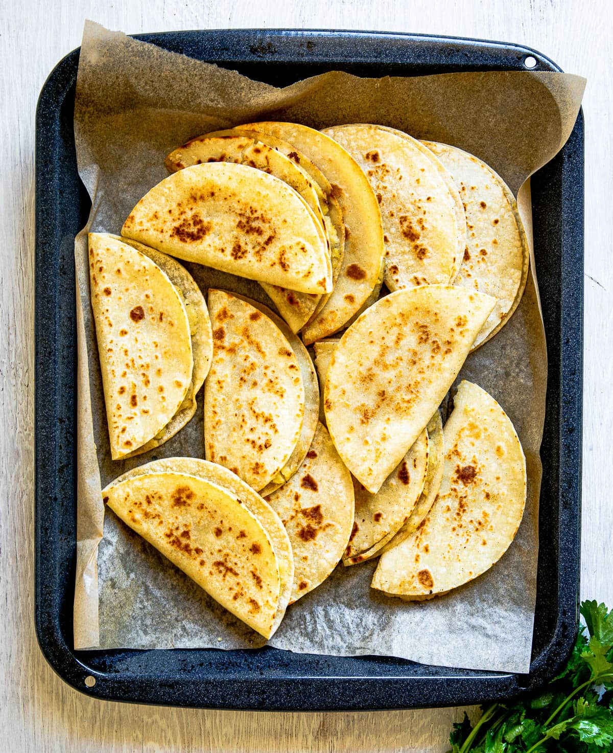 Tray of deep-fried corn taco shells overlapping each other on parchment paper, illustrating how to make fried taco shells.