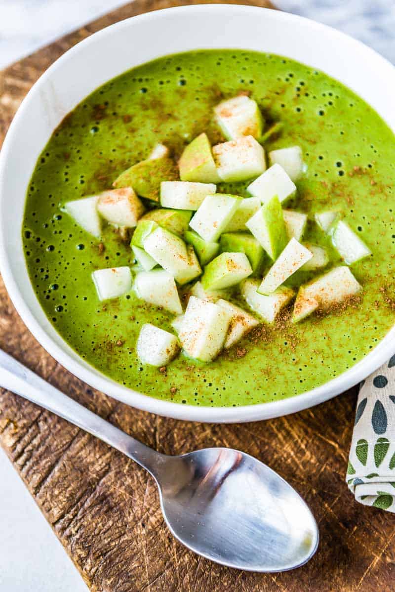 Healthy green smoothie bowl topped with sliced apples and cinnamon.