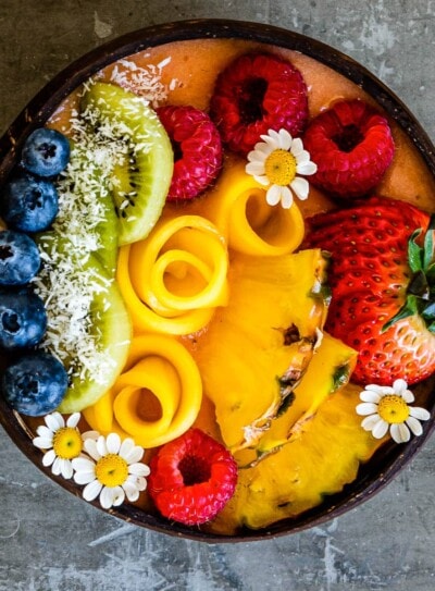 tropical smoothie bowl topped with fresh fruit and flowers.