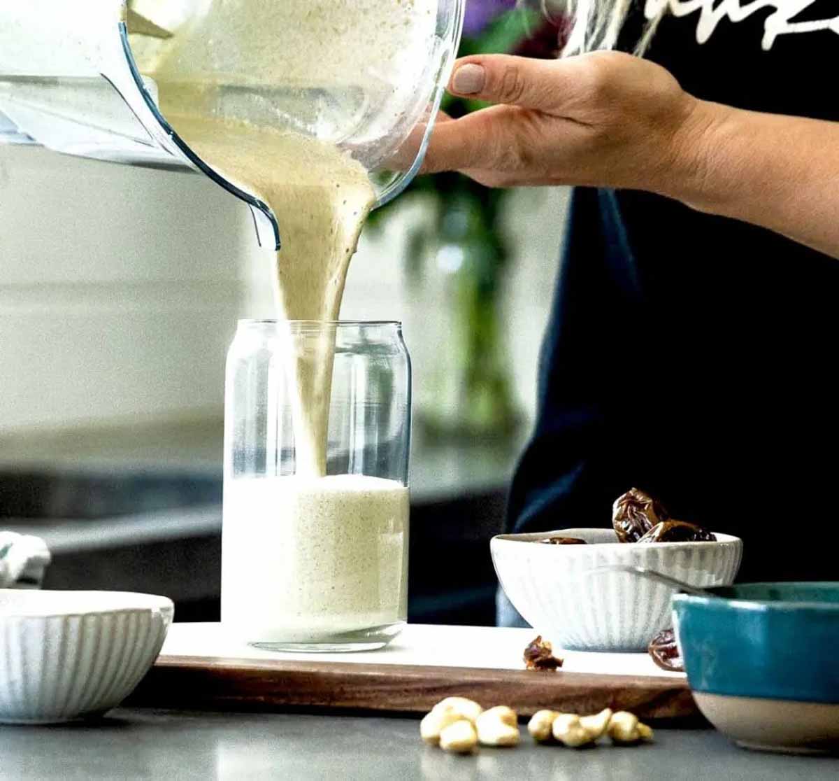 vanilla protein shake being poured into glass on counter next to white bowl of dates.