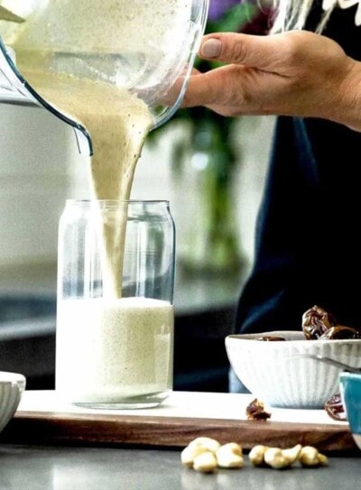 blender container pouring vanilla protein shake into glass on kitchen counter.