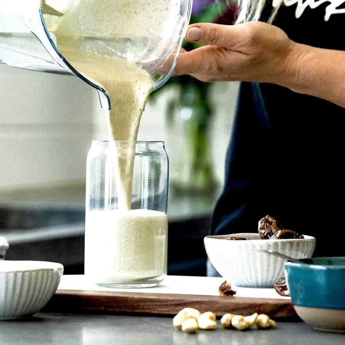 blender container pouring vanilla protein shake into glass on kitchen counter.