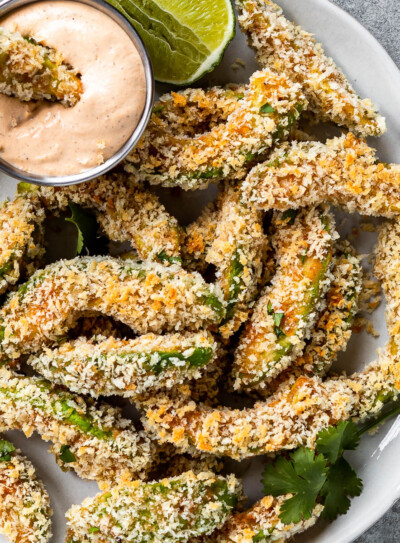 vegan avocado fries on a white plate with a container of chipotle ranch dipping sauce.