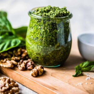 vegan basil pesto in a glass jar surrounded by basil and walnuts.