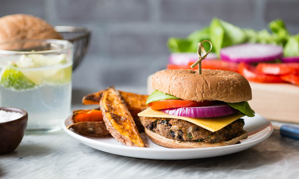 vegan black bean burger with toppings and sweet potato fries on a white plate.