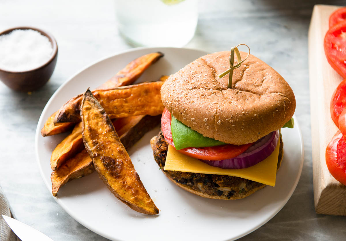 loaded plant-based burger on a plate with sweet potato fries.