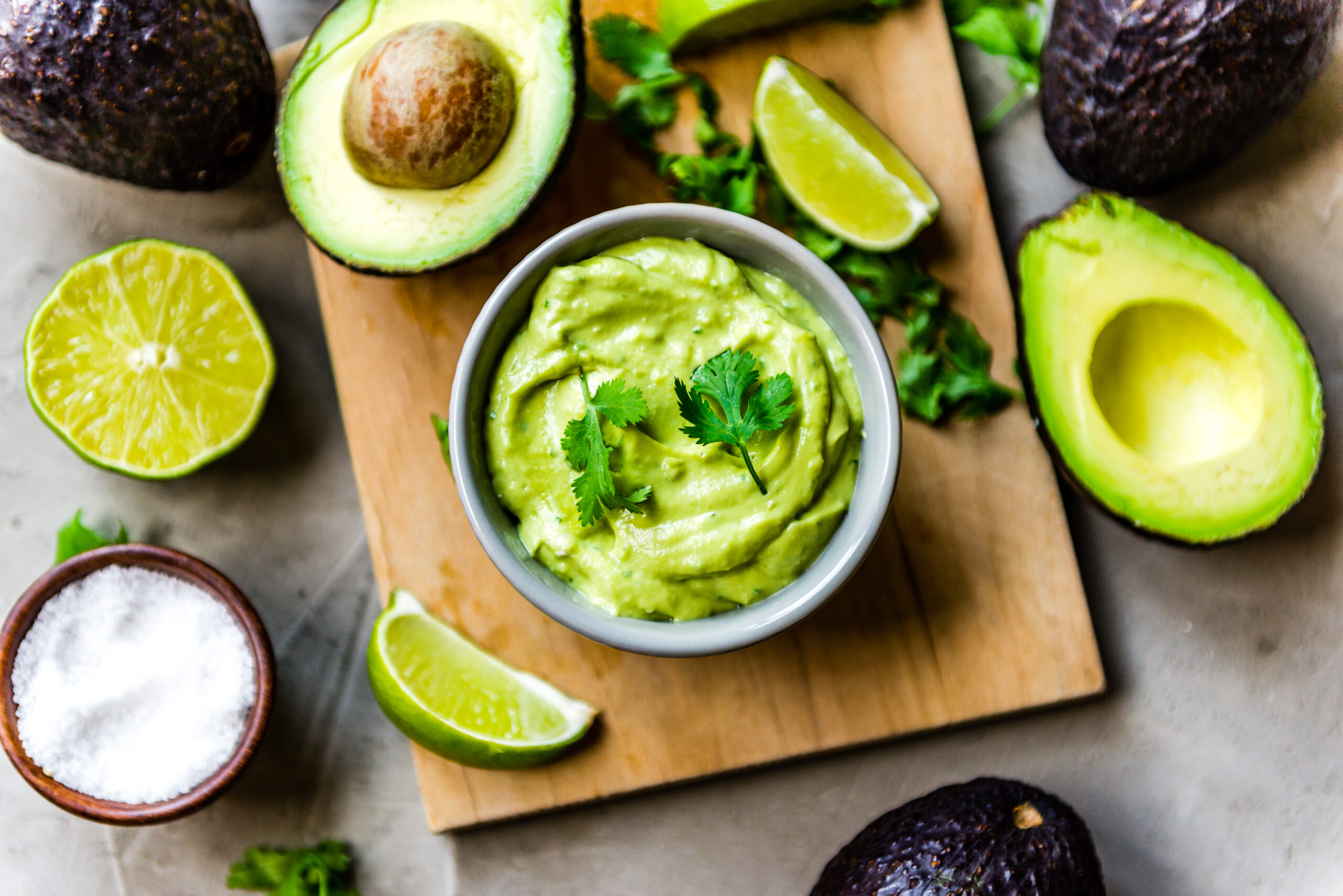 avocado crema in a small bowl surrounded by limes, avocado and sea salt.