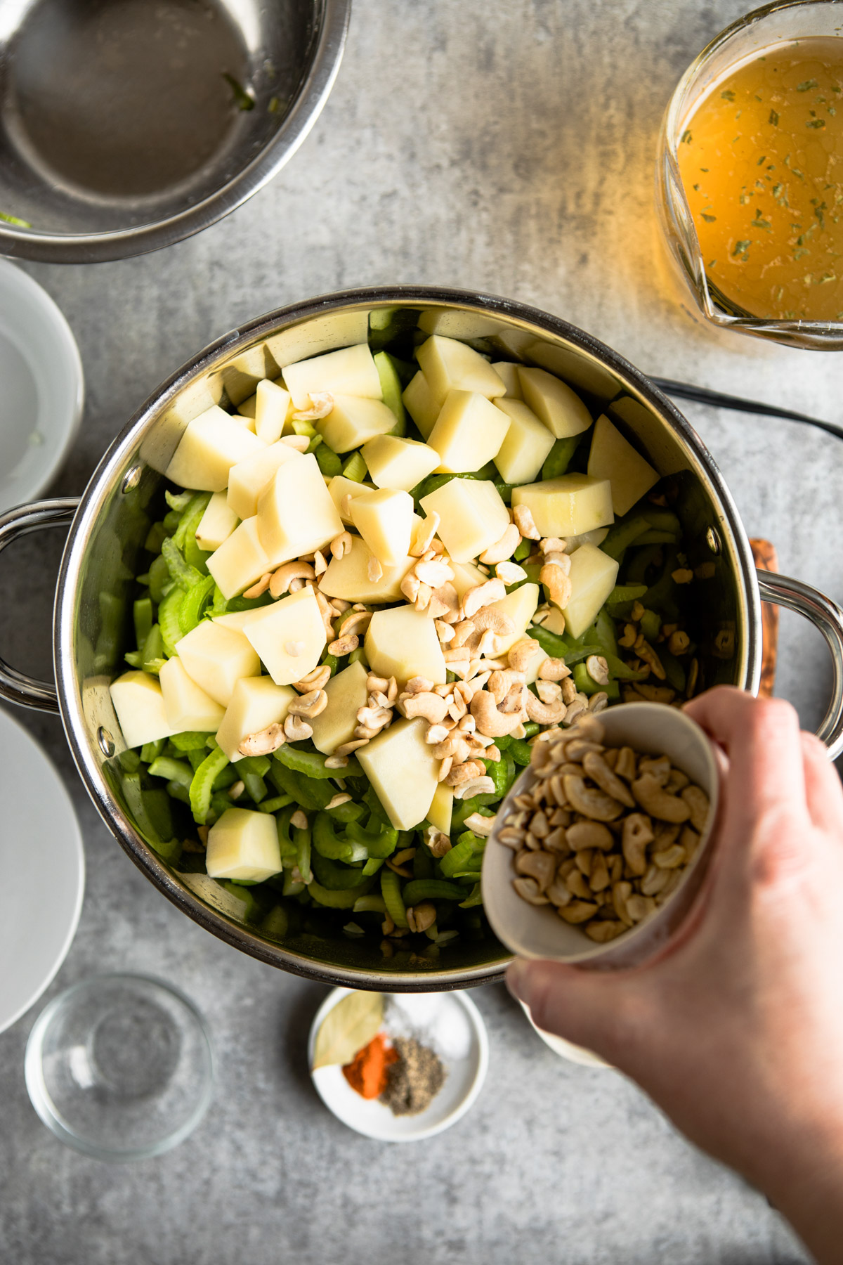 Pouring cashews into pot with potatoes and celery.