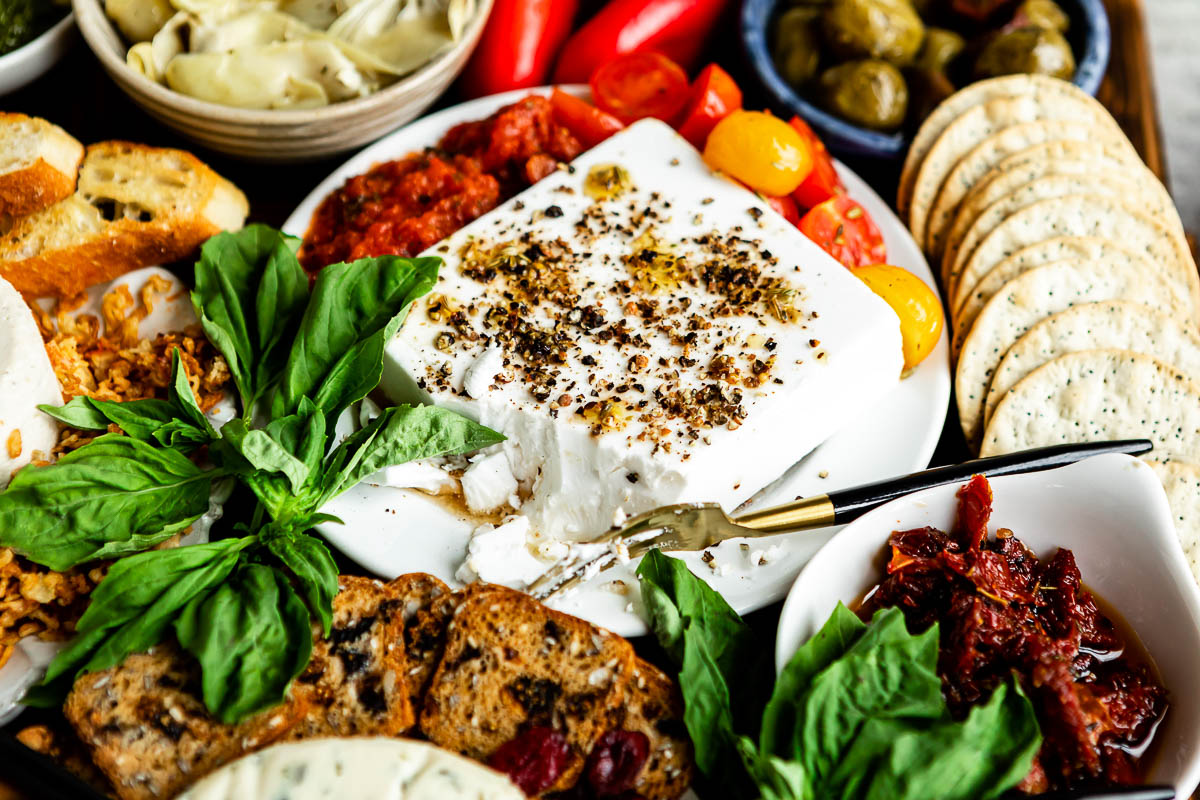 vegan feta topped with herbs and olive oil, surrounded by other colorful fruits and veggies.