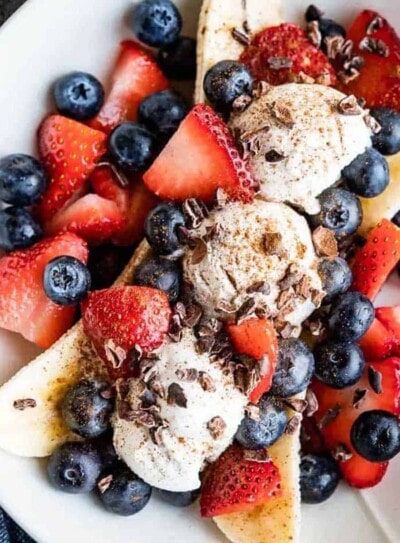 banana split with 3 scoops of ice cream in between a banana sliced in half lengthwise and topped with fresh strawberries, blueberries and cacao nibs.