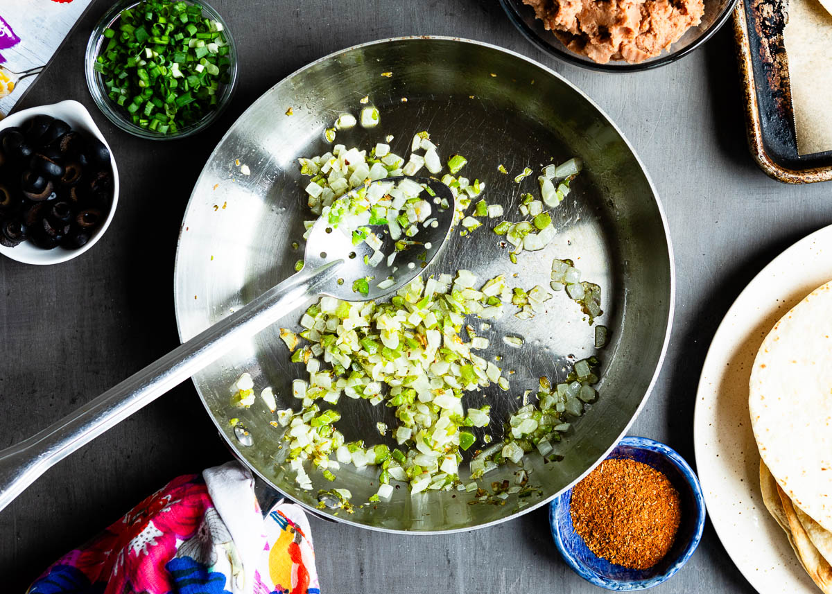 stainless steel skillet and slotted spoon with sautéd vegetables.