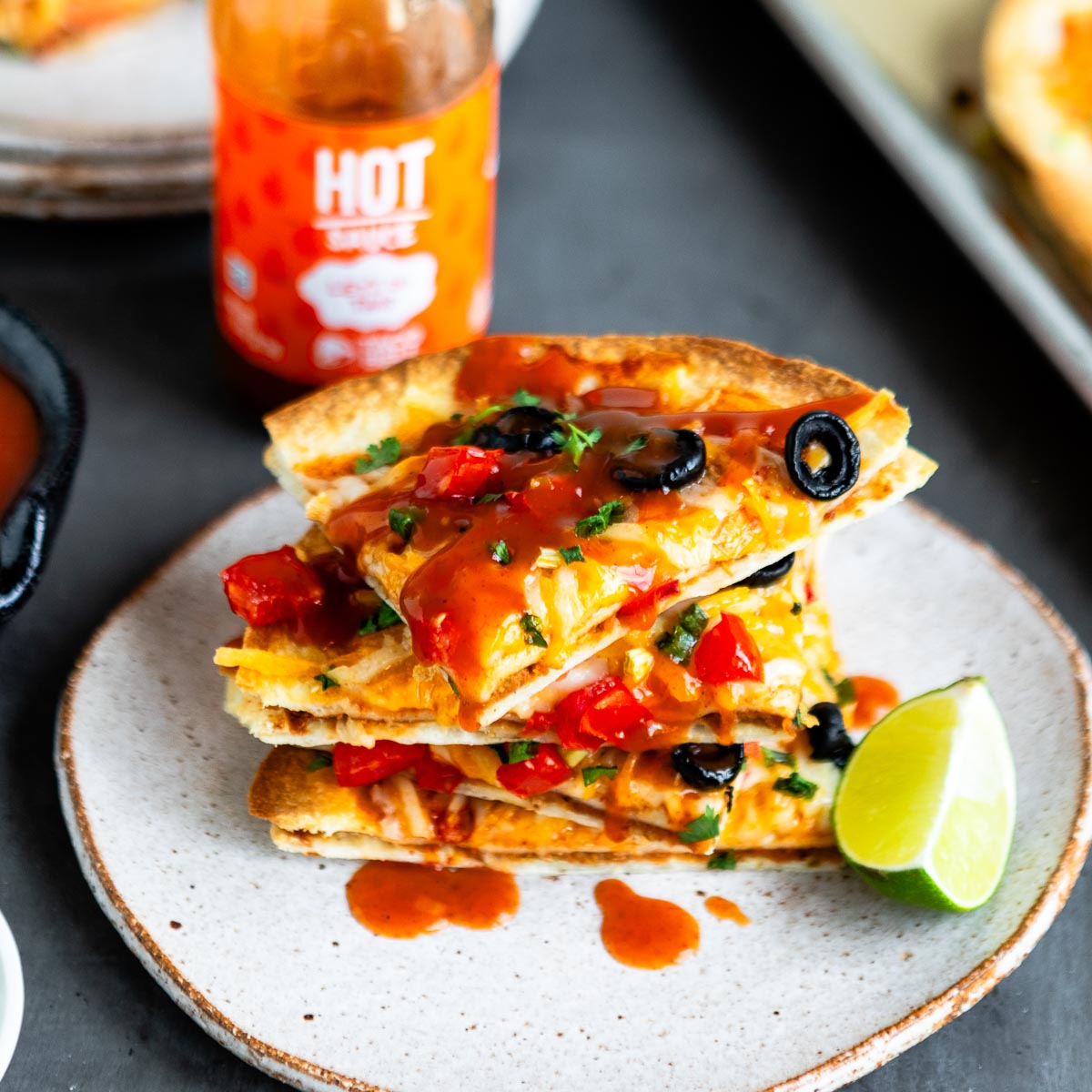 stacked slices of Vegan Mexican Pizza on stone plate next to a bottle of Taco Bell Hot Sauce.