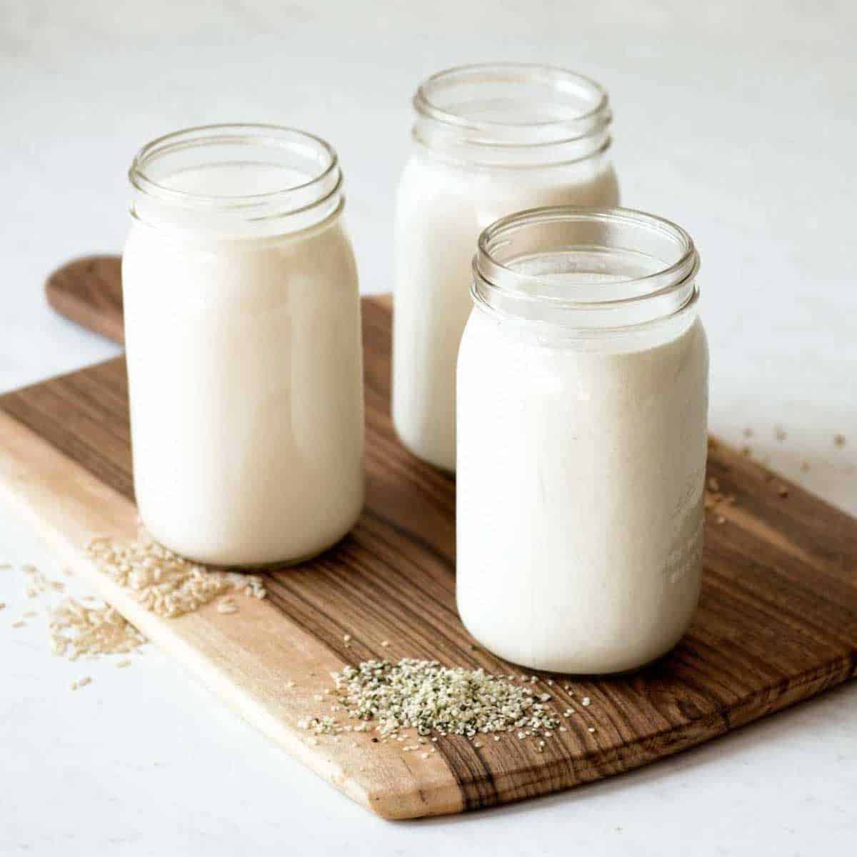 dairy free milks in glass jars on a wooden cutting board.