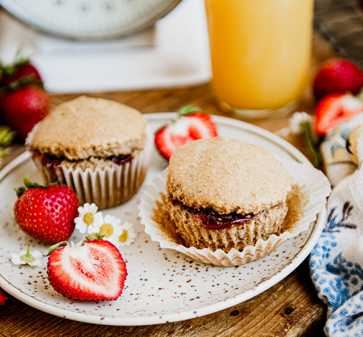 2 vegan muffins filled with strawberry jam on a white speckled plate.