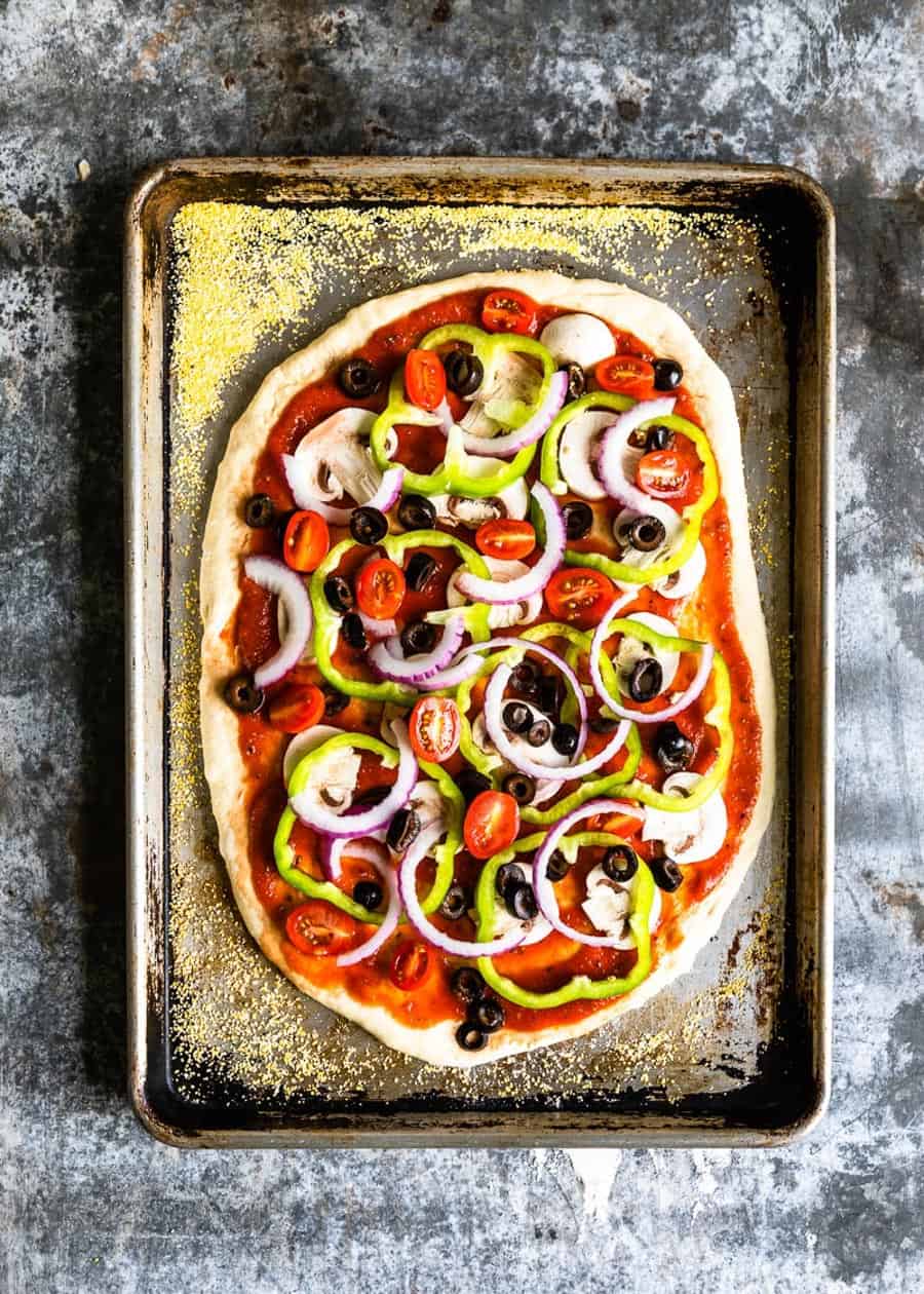 unbaked pizza on a baking tray on top of cornmeal.