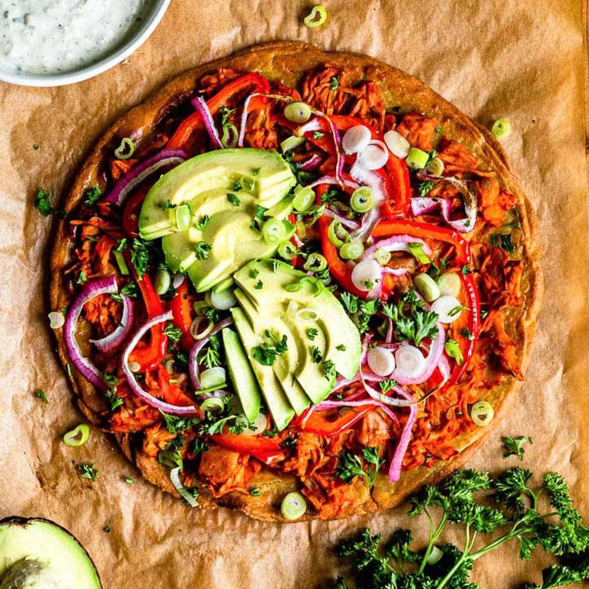 buffalo jackfruit pizza topped with fresh avocado and parsley.